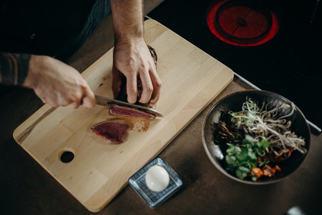 person using a cooks knife cutting meat on a wooden cutting board